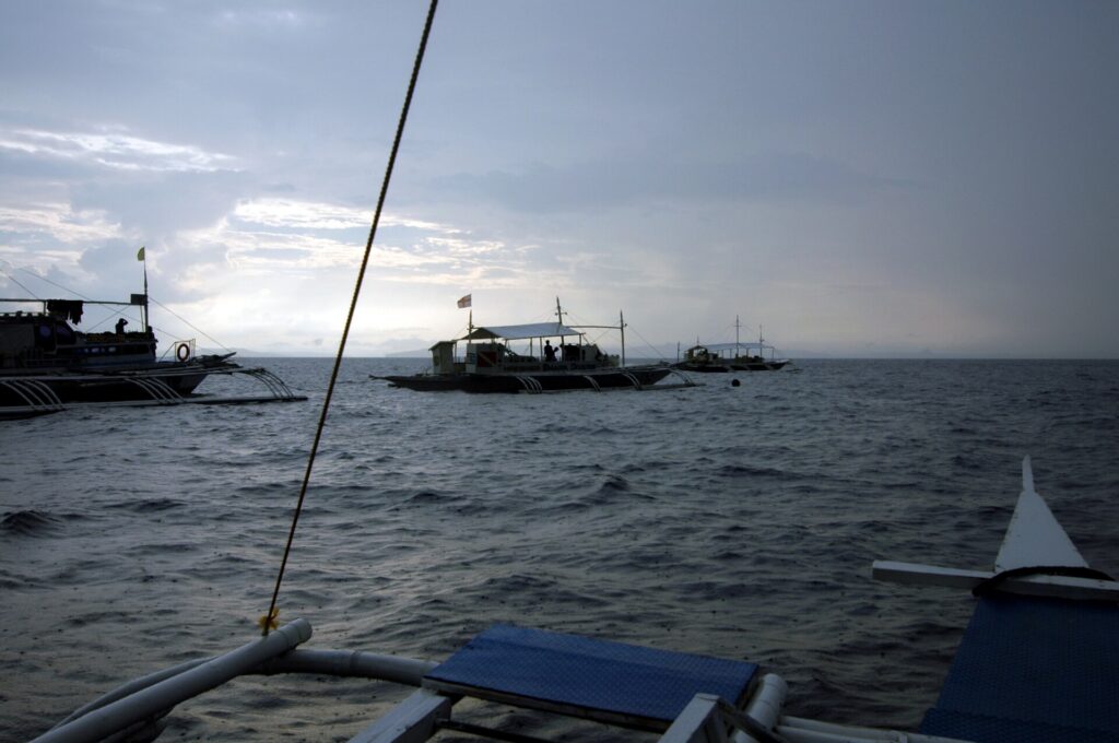 Trois bancas de plongée au mouillage sur Monad Shoal sous un ciel gris de petit matin, vues depuis le pont d'un autre bateau