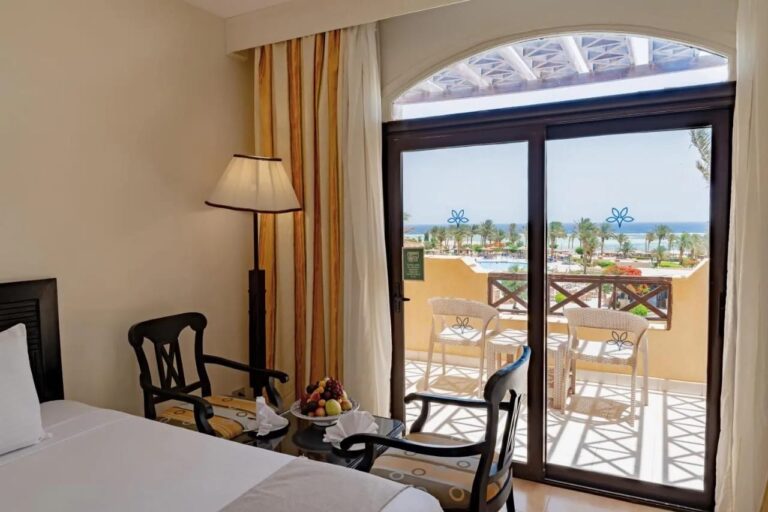 Une chambre avec deux fauteuils en bois sombre, ouverte sur un balcon face à la piscine et à la mer