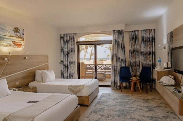 Une chambre à deux lits avec deux fauteuils bleus et une porte vitrée sur le balcon