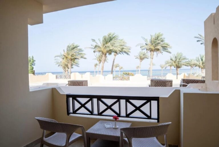 Un balcon avec deux chaises et une petite table, face aux palmiers et à la mer