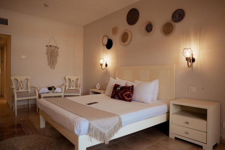 Une chambre au grand lit avec des paniers tressés au mur et deux chaises blanches
