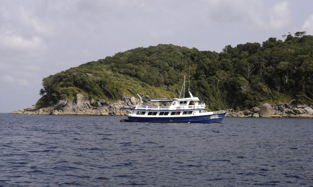 Un bateau de croisière bleu et blanc mouillé devant une île des Similan, ses blocs de granit gris au ras de l'eau sous la forêt