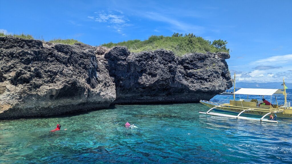 La falaise calcaire grise et creusée de l'île de Pescador, deux nageurs avec masque et tuba et une banca jaune dans une eau turquoise