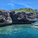 La falaise calcaire grise et creusée de l'île de Pescador, deux nageurs avec masque et tuba et une banca jaune dans une eau turquoise