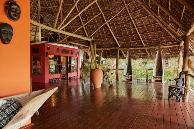 Un grand espace ouvert sous un toit de paille, avec un plancher en bois et des masques africains