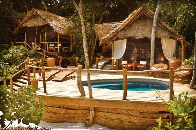 Deux bungalows au toit de paille et une terrasse en bois avec un bassin et deux transats