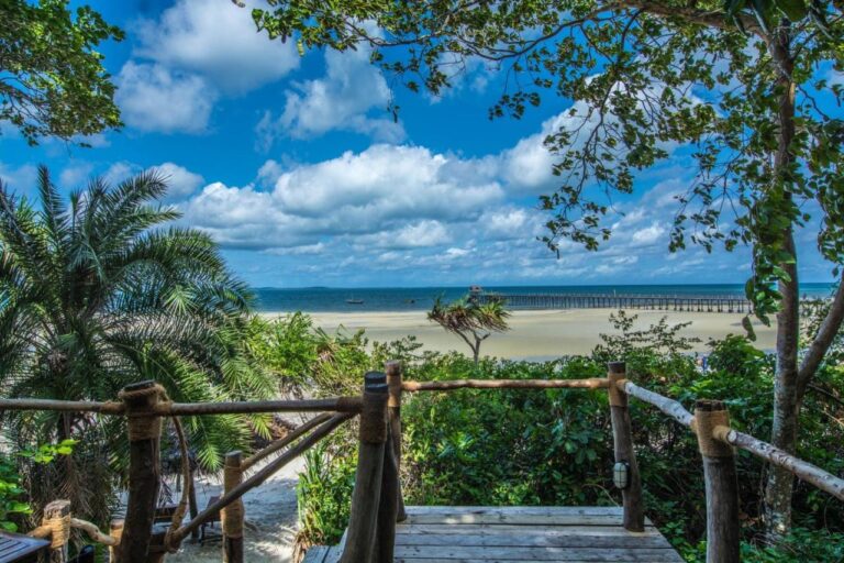 Vue d'une terrasse en bois sur une large plage de sable et un long ponton