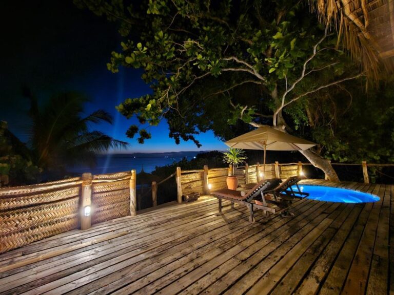 Une terrasse en bois éclairée le soir, avec un bassin, deux transats et un parasol