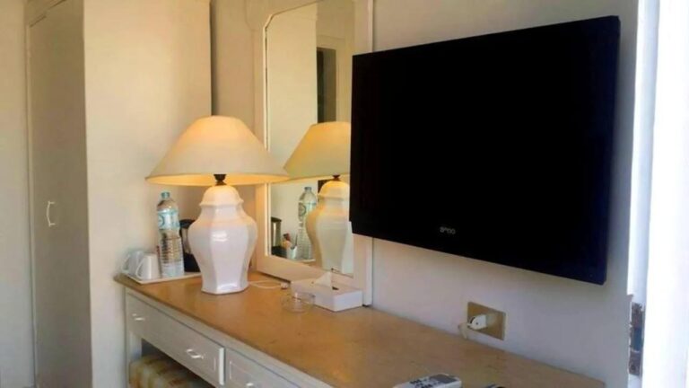 Une commode avec une lampe blanche, un miroir et une télévision murale
