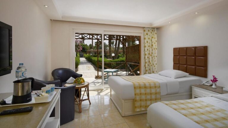Une chambre à deux lits avec deux fauteuils noirs, ouverte sur une terrasse et le jardin