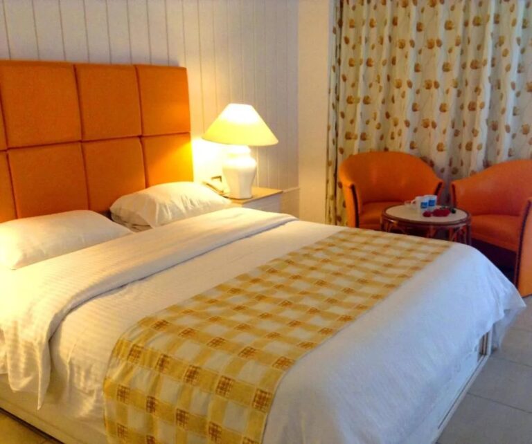 Un grand lit à tête de lit orange, avec deux fauteuils orange et une petite table ronde