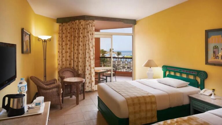 Une chambre aux murs jaunes avec deux lits et un balcon face à la mer