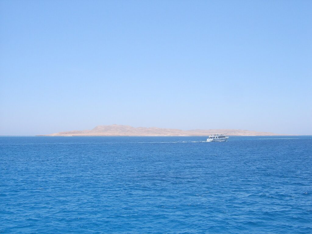 L'île plate et désertique de Giftun Soraya vue de la mer, un bateau de plongée blanc qui passe devant