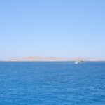 L'île plate et désertique de Giftun Soraya vue de la mer, un bateau de plongée blanc qui passe devant