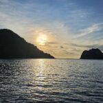 L'île Cocos en contre-jour au coucher du soleil, un bateau de croisière au mouillage à droite, la mer calme