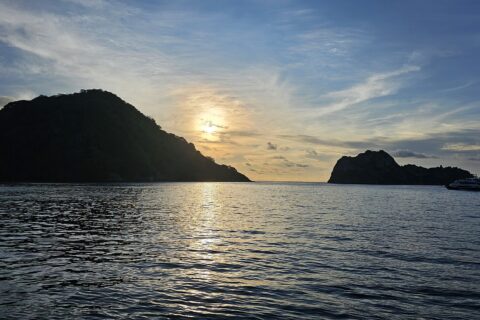 L'île Cocos en contre-jour au coucher du soleil, un bateau de croisière au mouillage à droite, la mer calme