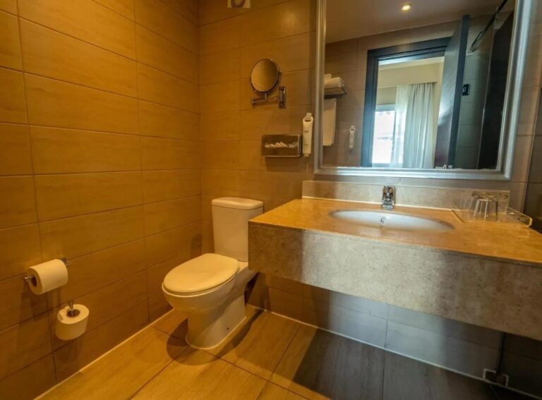Une salle de bains carrelée avec toilettes, vasque et grand miroir