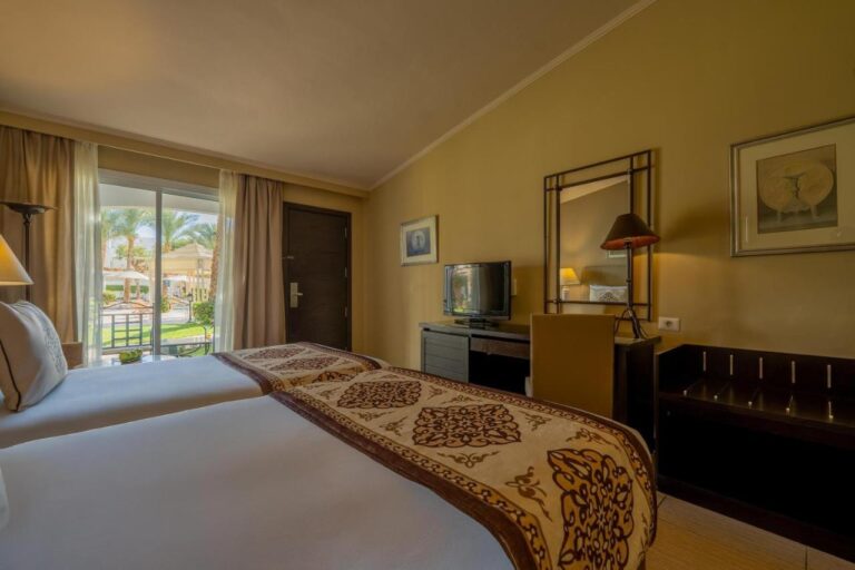 Une chambre à deux lits avec une porte-fenêtre sur le jardin et les palmiers