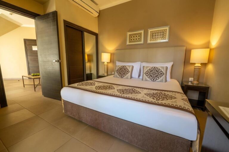 Une chambre au grand lit avec une penderie à miroir et une porte ouverte sur une autre pièce