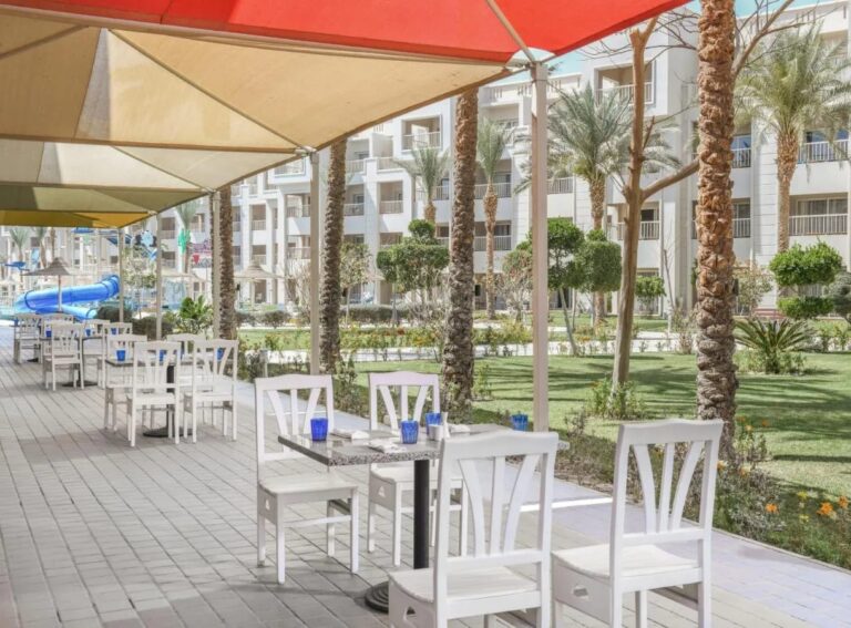 La terrasse d'un restaurant sous des voiles d'ombrage, face au jardin et aux palmiers