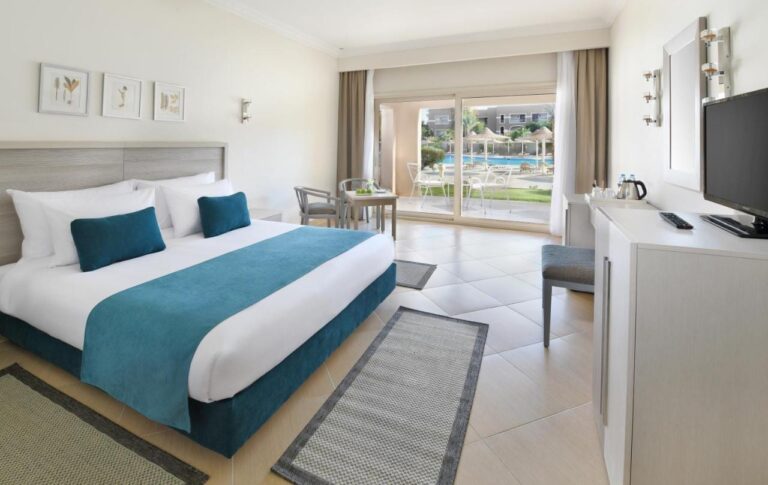 Une chambre au grand lit aux meubles clairs, ouverte sur une terrasse face à la piscine