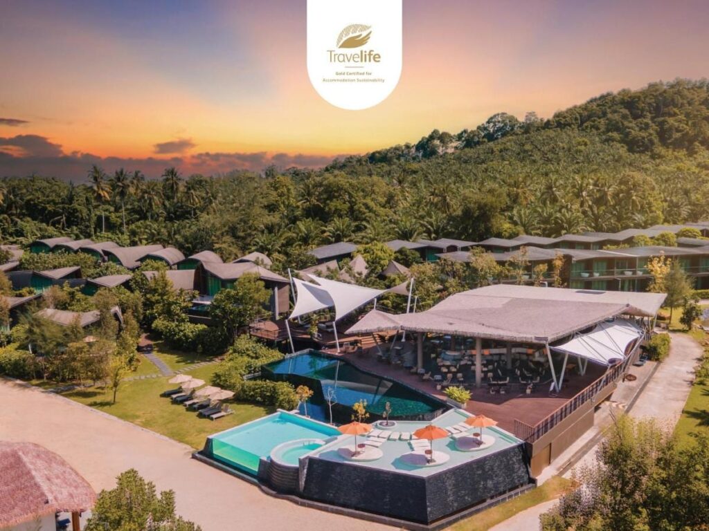 Vue aérienne du Kalima Resort Khao Lak au coucher du soleil, ses piscines et ses toits courbes au pied d'une colline boisée