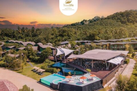 Vue aérienne du Kalima Resort Khao Lak au coucher du soleil, ses piscines et ses toits courbes au pied d'une colline boisée