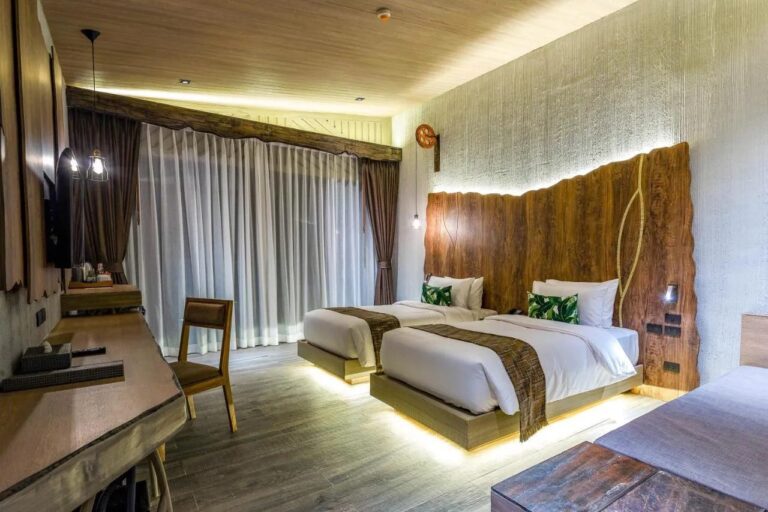 Une chambre à deux lits éclairés par en dessous, avec un bureau et des voilages