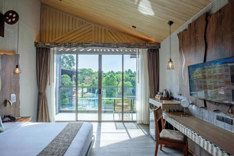 Une chambre sous un plafond en bois, ouverte sur un balcon qui donne sur la piscine