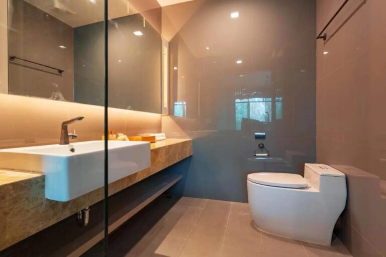 Une salle de bains avec une vasque sur un plan en marbre, un miroir éclairé et des toilettes