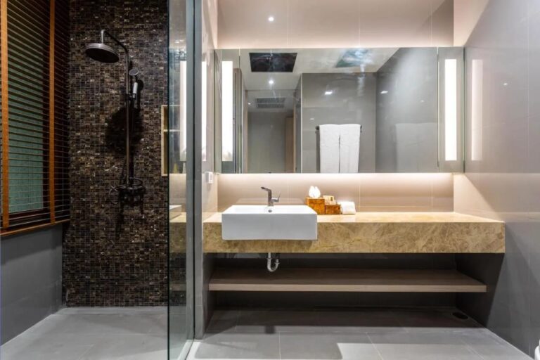 Une douche contre un mur en mosaïque sombre, à côté d'une vasque sous un miroir éclairé