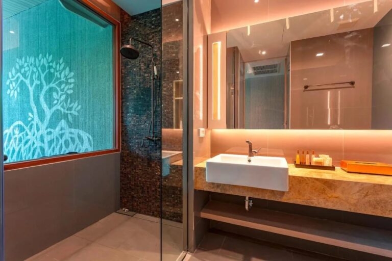 Une douche derrière une paroi vitrée, près d'une fenêtre décorée d'un arbre