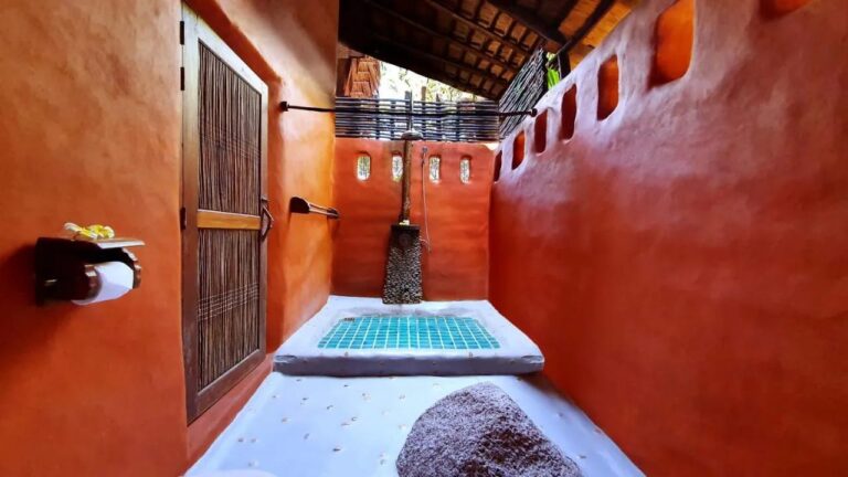 Une salle de bains semi-ouverte aux murs orange, avec une douche sur un sol en mosaïque turquoise