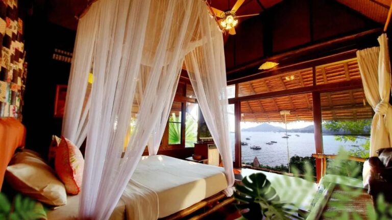 Une chambre au lit sous moustiquaire, ouverte sur la baie et les bateaux