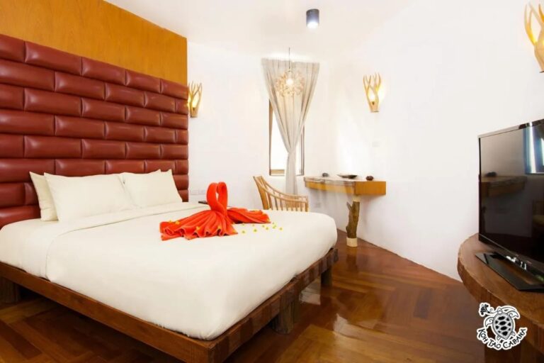 Une chambre blanche du Koh Tao Cabana, avec un grand lit, une tête de lit rouge capitonnée et une télévision