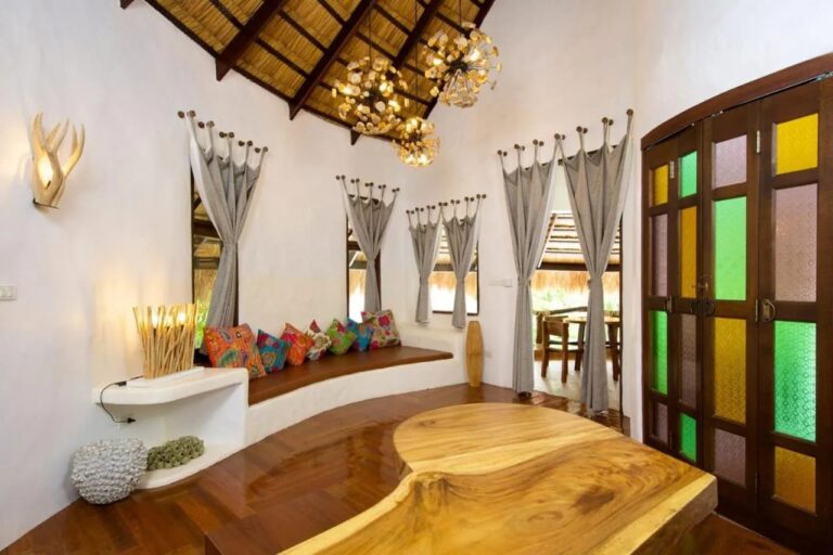Un salon blanc avec une banquette aux coussins colorés, une table en bois massif et des portes à vitraux