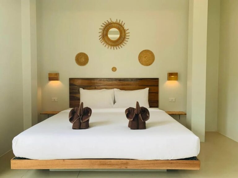 Un grand lit à tête de lit en bois, avec des éléphants en serviettes et un miroir soleil en rotin
