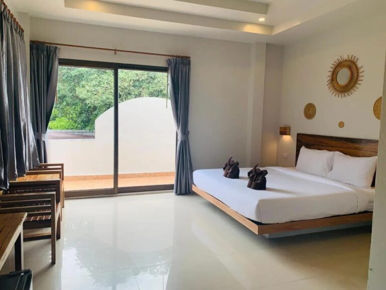 Une chambre au grand lit avec une baie vitrée sur un balcon et des fauteuils en bois