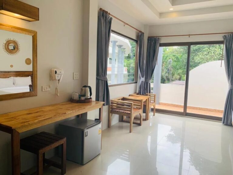Un bureau en bois avec une bouilloire et un petit réfrigérateur, près de la baie vitrée du balcon