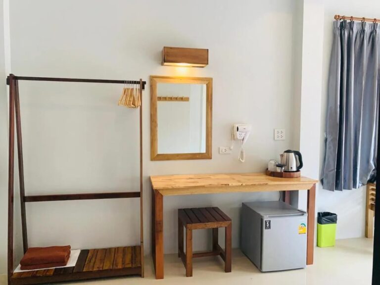 Un portant en bois, un miroir et un bureau avec une bouilloire au-dessus d'un petit réfrigérateur