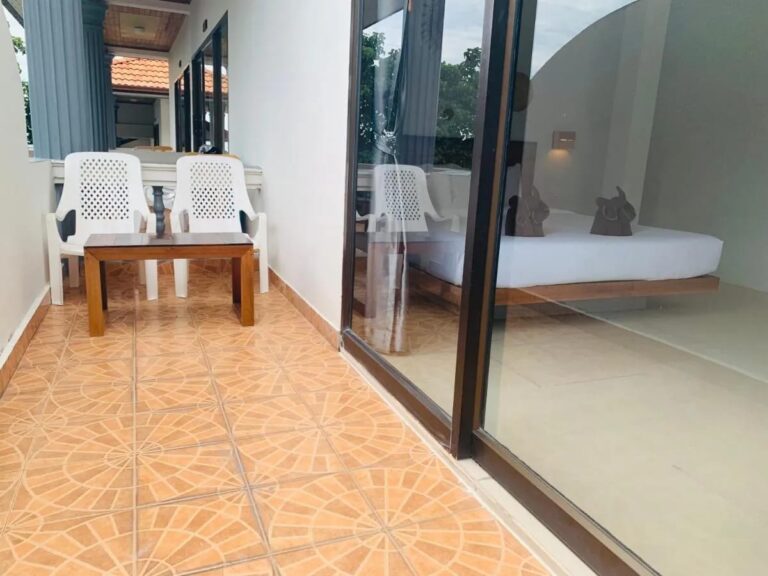 Un balcon carrelé avec deux chaises blanches et une table basse, devant la baie vitrée d'une chambre
