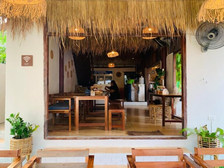 La salle du restaurant, avec ses tables en bois et ses suspensions en rotin