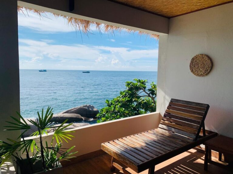 Une terrasse couverte avec une chaise longue en bois, face à la mer et aux rochers