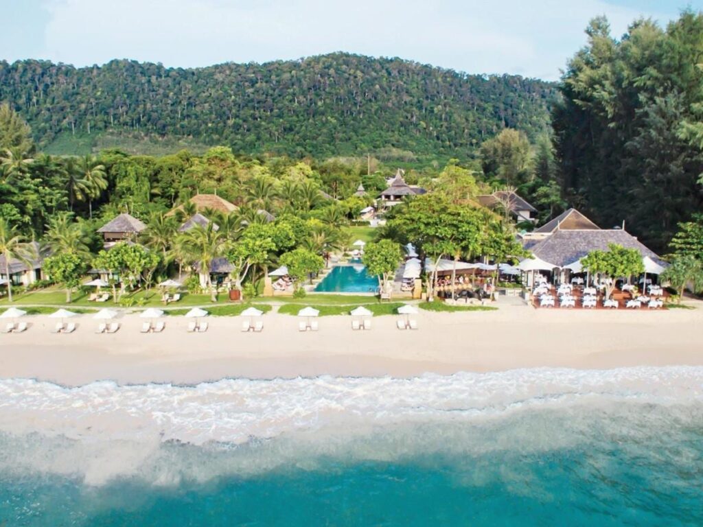 Le Layana Resort vu de la mer, avec sa plage, ses parasols blancs, sa piscine et ses toits sous les palmiers