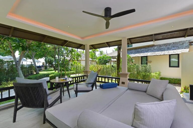 Une terrasse couverte avec un grand lit de repos, deux fauteuils et un ventilateur au plafond