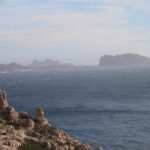 Depuis les rochers calcaires du Frioul au premier plan, vue sur une mer agitée et moutonnante jusqu'à l'île Maïre et la côte des Goudes, découpées dans la brume.