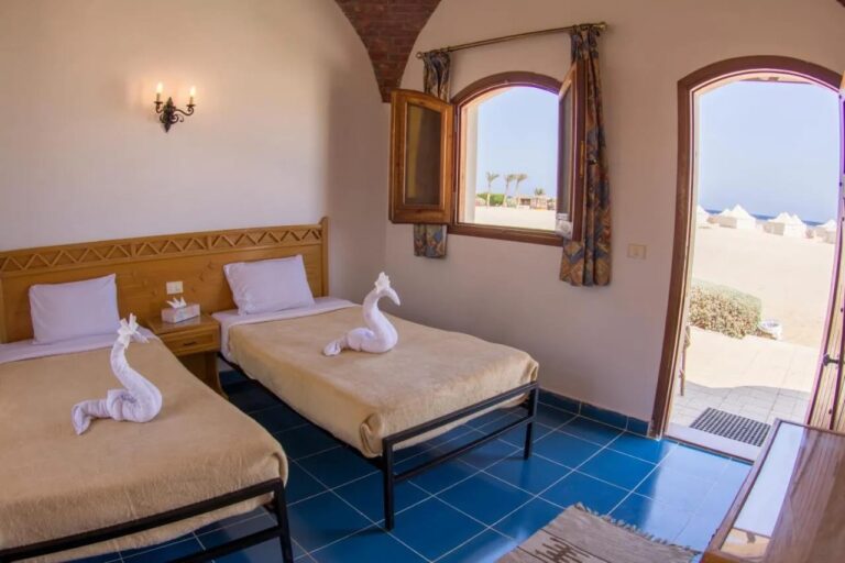 Une chambre à deux lits sous une voûte en brique, avec la porte ouverte sur le sable