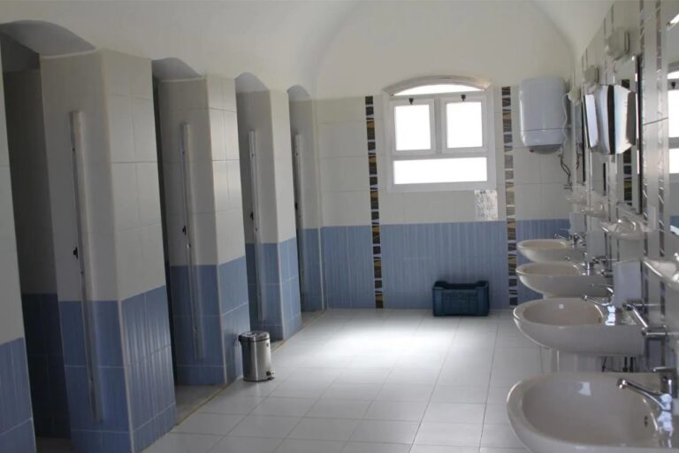 Un bloc sanitaire avec des cabines alignées et une rangée de lavabos