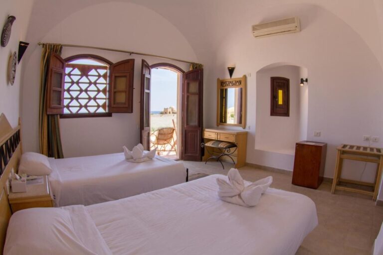Une chambre à deux lits sous une voûte blanche, avec la porte ouverte sur une terrasse et la mer