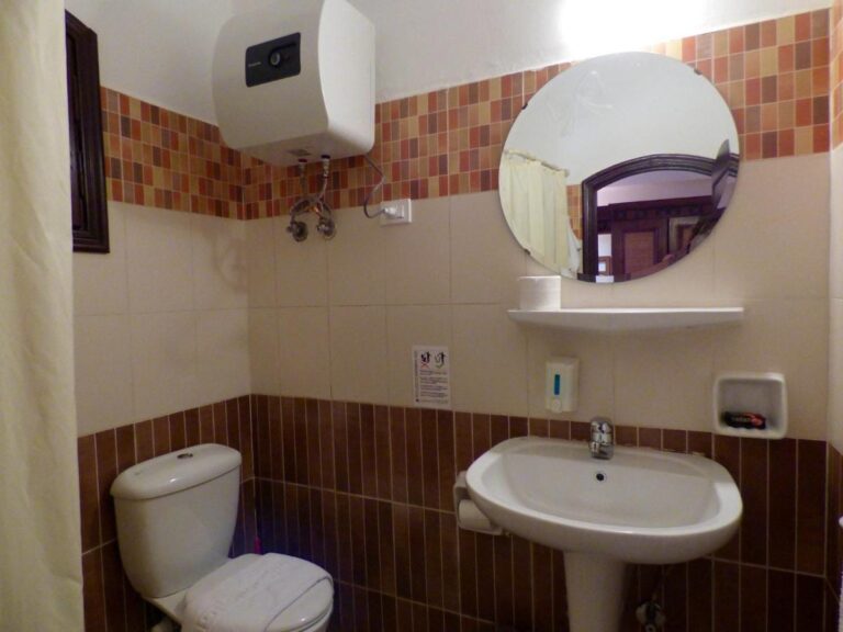 Une salle de bains avec lavabo, toilettes, miroir rond et chauffe-eau